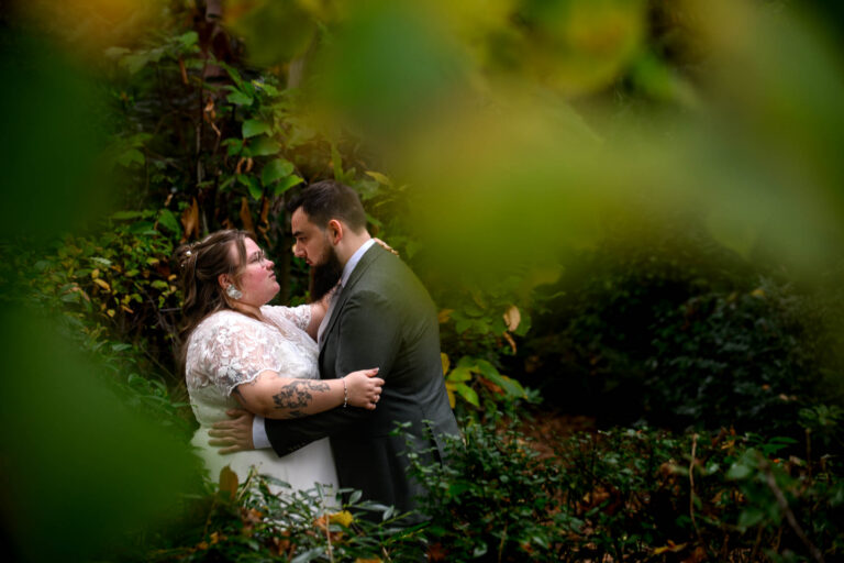 Bruid en bruidegom omhelzen elkaar in een weelderige, groene tuin omringd door gebladerte.